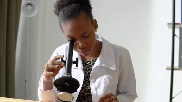 African Female Scientist Doing Some Research and Looking Through a Microscope in Laboratory