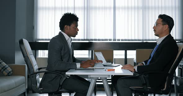 Two Young Businessman Talking at Desk in Office