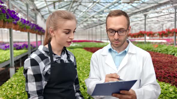 Professional Female Farmer Discussing Working with Agricultural Engineer Surrounded By Fresh Plant