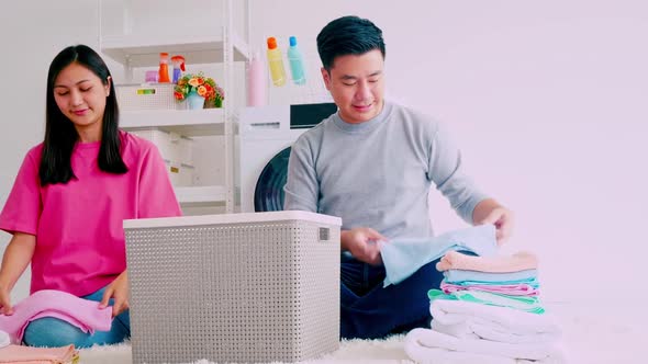 Husband helping his wife folding clothes. Happy Asian couple spending time together at home.