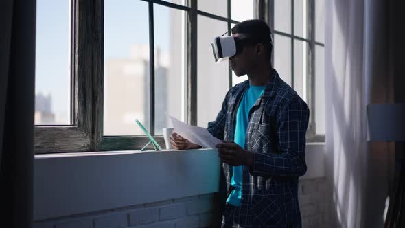Side View of Young Satisfied African American Man in Pajamas and VR Headset Holding Business Graph