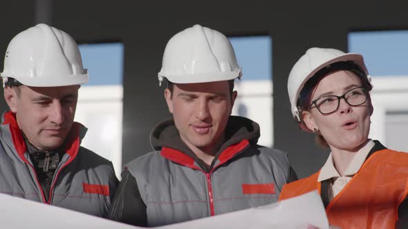 Friendly Team Male and Female Experts in the Construction Industry Safety Helmets Discuss Drawings