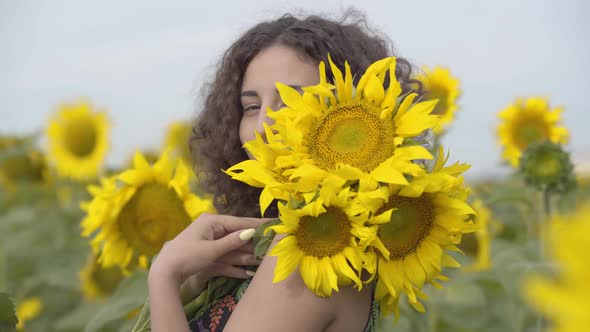 Portrait of Pretty Curly Playful Girl Looking at the Camera Smiling Standing in the Sunflower Field