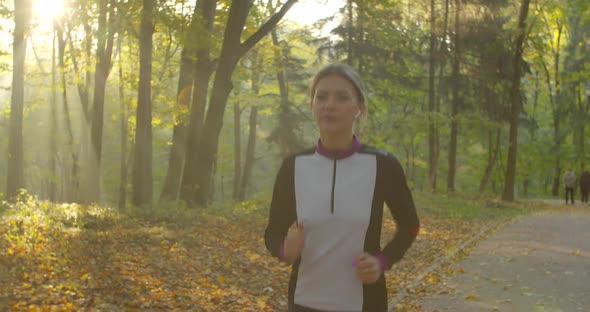 Young Attractive Woman Listening Music in the Earphone While Running in the City Park