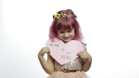 Child Girl Princess Holds Pink Paper Heart with Text About Mother. Mother's Day