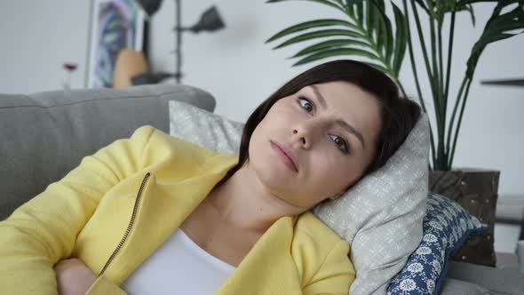 Serious Young Woman Looking at Camera while Laying on Sofa at Home