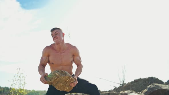Muscular man with trained body exercises with stones. Strong bodybuilder doing workout by throwing h