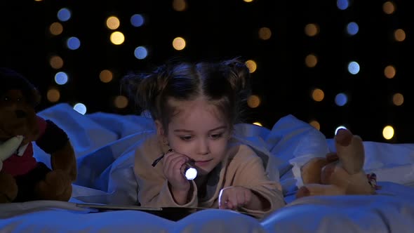 Little Girl at Night Reading a Book on the Bed. Bokeh Background. Slow Motion