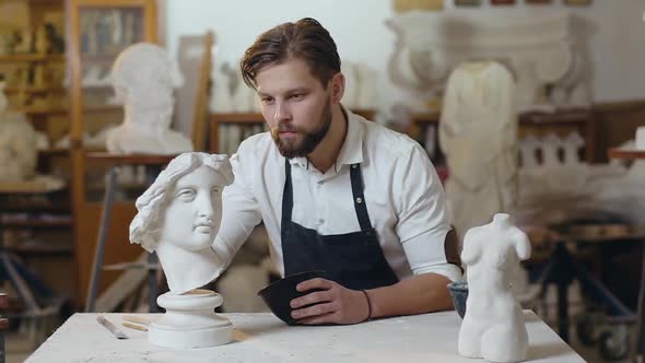 Young Modern Bearded Sculptor Carefully Applying the Glue to the Sculpture Head