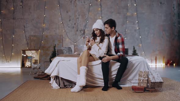 Young Couple Responding To Christmas Messages Sitting on the Bed in the Living Room,