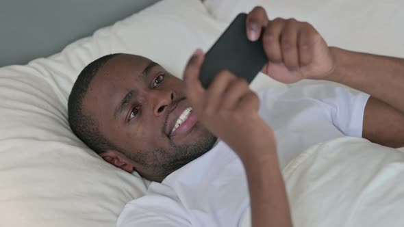 African Man Playing Game on Smartphone in Bed