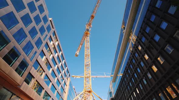 A Large Tower Crane in the Downtown of the Modern City. Glass Office Buildings Around. Low Angle
