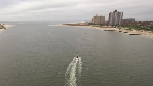 An aerial view over East Rockaway Inlet as a boats head out to sea leaving a white wake behind. The