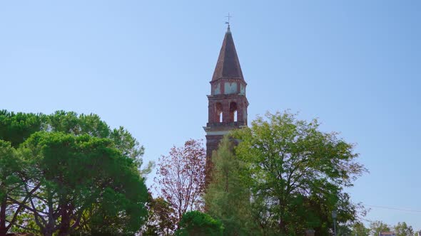High Church Bell Tower with Brick Fence Stands Among Park