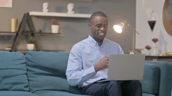 African Man Talking on Video Call on Laptop on Sofa