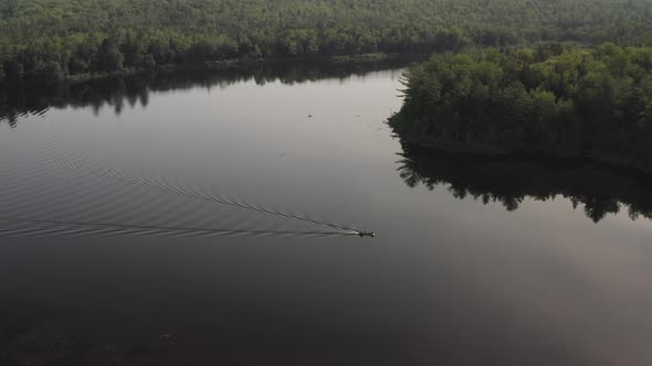 Static aerial shot over flat calm lake lake boat travels across surface surrounded by wilderness