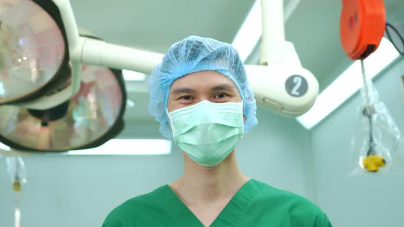 Portrait of Asian surgeon with medical mask standing in operation theater at a hospital. Team of Pro