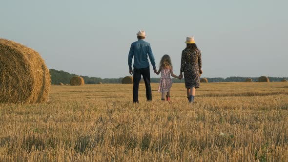 Family of Three Walking in a Field with Haystacks