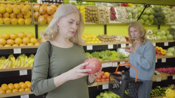 Portrait of Mature Caucasian Woman Advising with Friend on Purchase of Juicy Organic Pomegranate