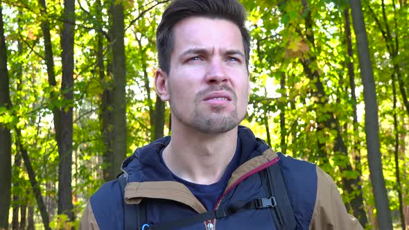 A Young Handsome Hiker Looks Confusedly at a Map in a Forest on a Sunny Day - Closeup