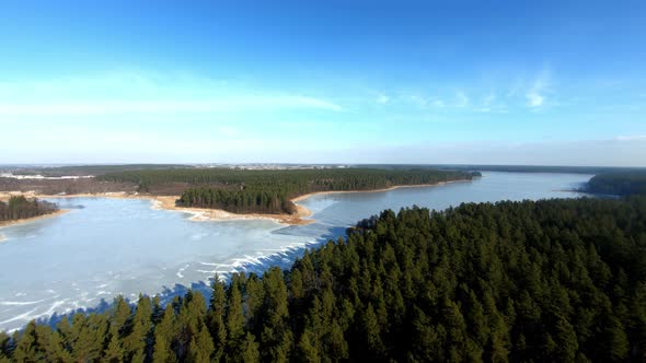 A beautiful aerial backward shot of a landscape with an enourmous frozen lake and spruce forest duri