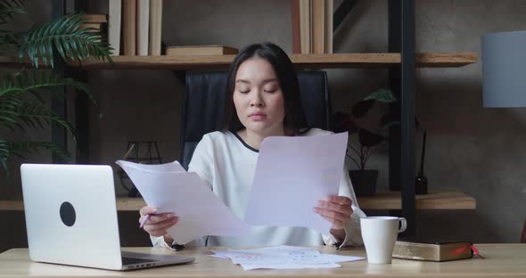 Stressed Unmotivated Asian Woman Confused By Mistake in Documents Looking Through Papers Frowning