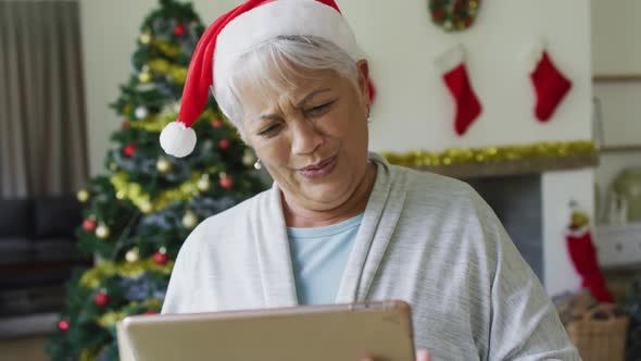 Happy mixed race senior woman in santa hat on video call on tablet at christmas time