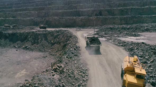 Mining Dump Trucks in Large Granite Open Pit Mine. Loaded Truck Rides on Road Quarry Ledge Aerial