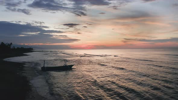 Aerial Flyby Silhouette of a Fishing Boat Sailing on Seawater with Waves Rolling Onto the Beach