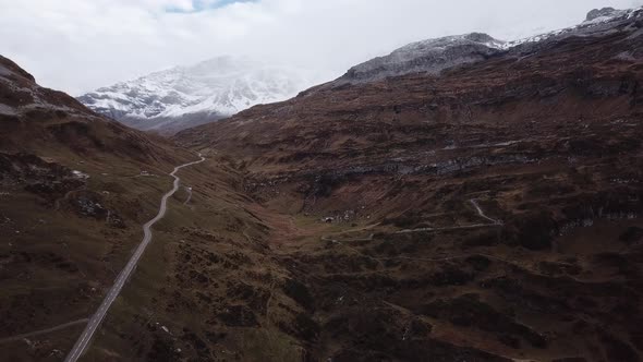 Aerial shot of a rocky mountain landscape criss-crossed by winding roads and snowy hills in the back