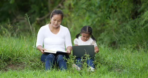 Mom reading a book and daughter using laptop