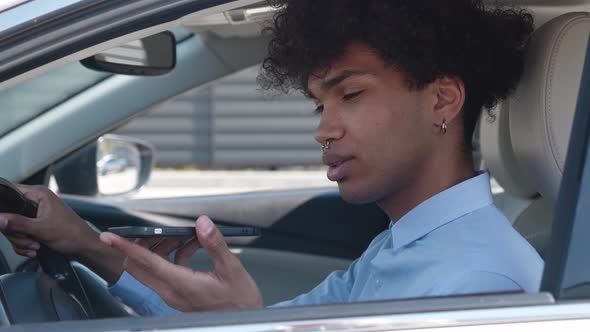 Happy Afro American Millennial Recording Voice Message on Smartphone in Modern Car