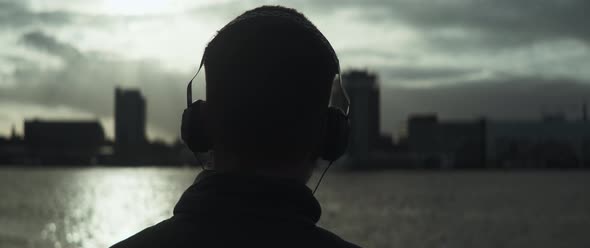 Back view of a man listening music in front of the river and slowly dancing