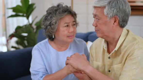 Asian senior elderly couple sitting on a sofa, woman giving hand to man, support, understanding.