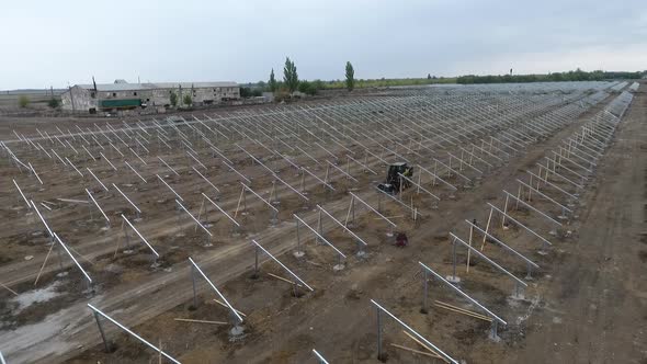 Workers with a Small Excavator Between the Solar Panel Mounting Racks