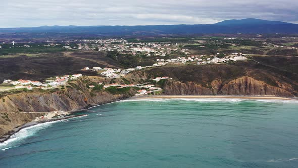 Praia da Arrifana beach in west Portugal with the town of Picao on top of terrain, Aerial pan right