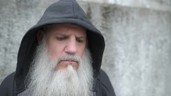 Serious Mature Bald Bearded Man with Hoodie Thinking Against Concrete Wall Outdoors