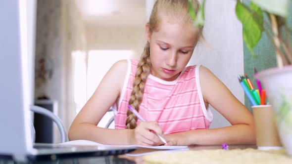 Caucasian Girl Doing Homework at Home in Front of a Laptop Writes in a Notebook