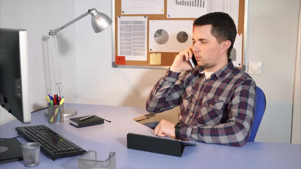 Office Worker Talking on a Mobile Phone with His Client Sitting in His Office.