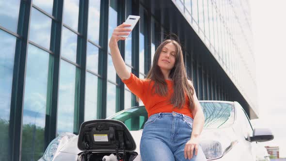 Woman Taking a Selfie While Charging an Electric Car Near a Mall