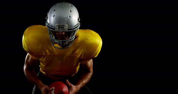 American football player leaning forward holding a ball