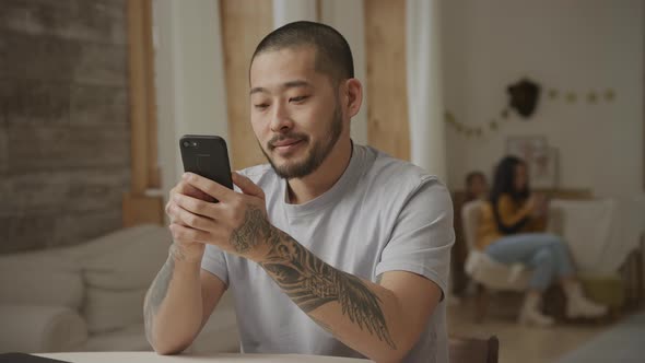 20s Tottoed Asian Father Swiping on His Smartphone with Various Facial Expressions