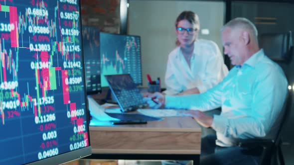 Monitors with Stock Rates and Two Stockbrokers Working Nearby