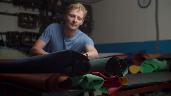 Craftsman Choosing Leather Material From Multicolored Rolls Indoors