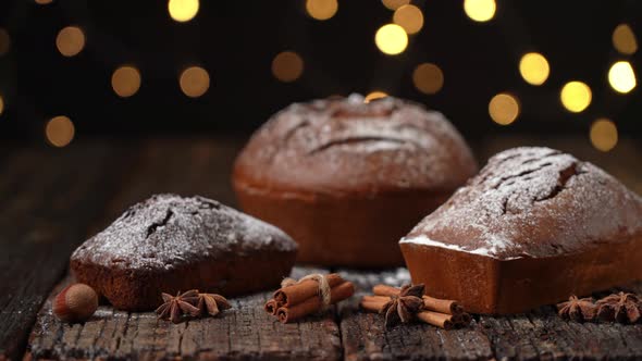 Three Christmas Bread Stollen on a Wooden Textured Table Against the Background of Blurred Lights in