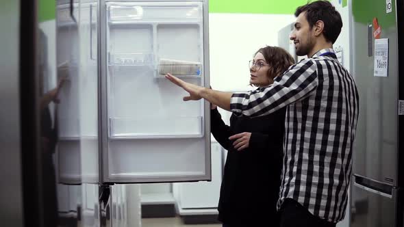 Young Married Couple Inspect Open Door Refrigerator Design and Quality Before Buying in a Consumer