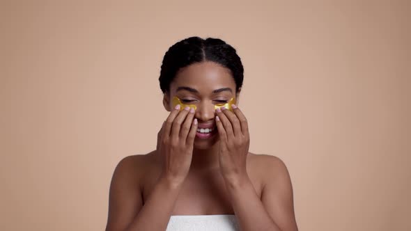 Young Pretty African American Woman Applying Golden Collagen Patches Under Eyes Making Light Massage