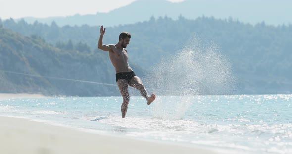 The Handsome Man with a Perfect Athletic Body in Swimming Trunks Having Fun on a Deserted Beach in