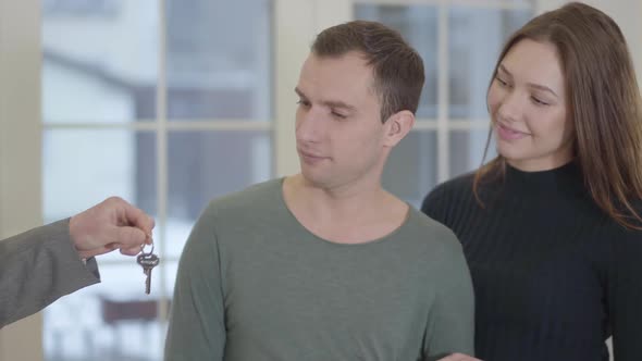 Portrait of a Happy Couple Receiving the Keys From an Unrecognized Real Estate Agent and Joyfully