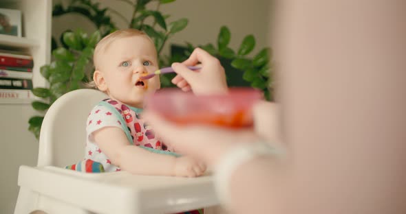 Little baby girl eating baby food on high chair with mother